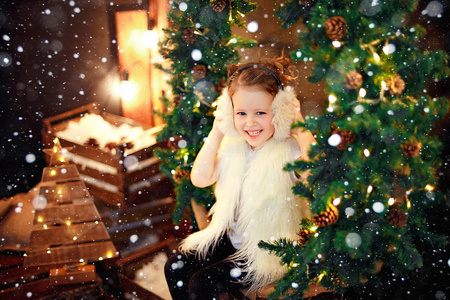 可爱的小女孩在毛皮耳坐在圣诞节树附近