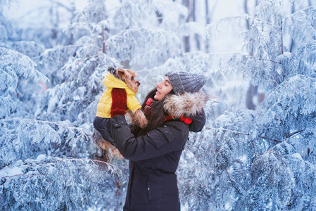 迷人的年轻女人在外面的雪地里和她的狗约克郡猎犬玩得很开心。 带着可爱狗的年轻女人