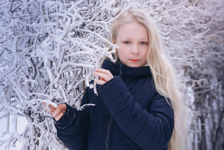 冬天的女孩吹雪。美丽快乐的青少年模特女孩在冬季公园玩得很开心。美丽的女孩在户外笑。享受大自然。