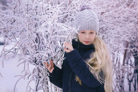 冬天的女孩吹雪。美丽快乐的青少年模特女孩在冬季公园玩得很开心。美丽的女孩在户外笑。享受大自然。