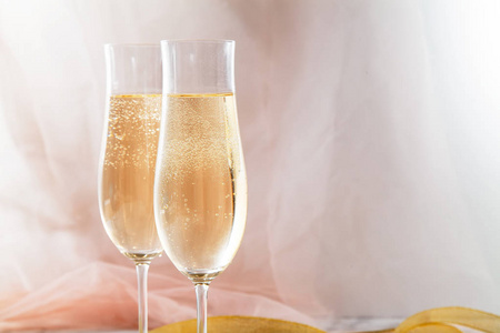 大理石背景上有两个带有香槟的长笛眼镜。 粉红色透明织物。 柔和的光线。 水平组成部分