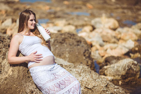 年轻的孕妇在山的背景下呼吸新鲜的海洋空气