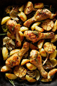 烤鸡腿与土豆楔形，大蒜，洋葱和芳香草药在烤盘顶部视图