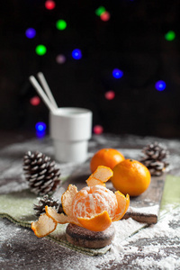 在一个白色的盘子上的新年餐桌上的橘子, 颠簸和一杯可可, 绿色的餐巾和新年的灯在黑暗的背景