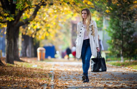 微笑的妇女在美丽的秋天街道上走在外套