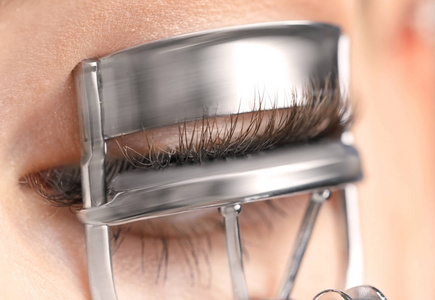 女人使用睫毛夹睫毛夹睫毛夹吃爆米花的年轻女人的肖像使用睫毛夹的