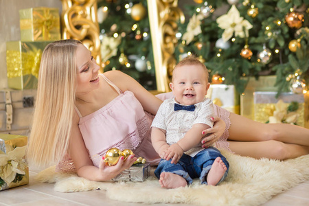 快乐的家庭母亲和宝宝的儿子在圣诞节假期玩家。与妈妈在载歌载舞装饰房间与圣诞树的幼儿。母亲和男婴的画像在休闲衣裳