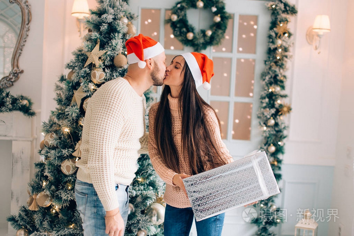 夫妇与礼物微笑轻轻拥抱在圣诞灯