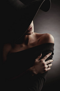 黑色画室肖像，优雅的女人戴着黑色宽帽和黑色连衣裙。隐藏着半张脸。
