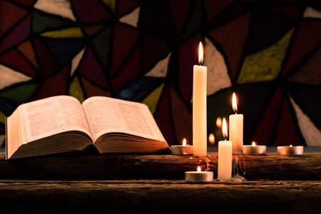 圣经和蜡烛在一张古老的橡木木桌上。 美丽的彩色玻璃窗背景。宗教概念。