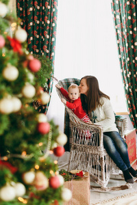 年轻漂亮的妈妈带着一个可爱的小男孩坐在柳条椅上, 在家里的装饰房间里。圣诞节好心情。新年。生活方式家庭和团结概念