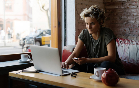 假男女孩坐在咖啡馆里，在现代便携式电脑的屏幕上阅读电子邮件。 年轻的自由职业者正在等待Skype的电话，同时在一家现代咖啡店吃早