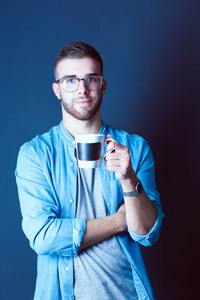英俊的年轻男子站在捧着一杯咖啡在他手中的画像