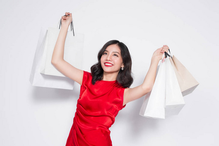 开朗时尚的亚洲女人，穿着红色连衣裙，购物袋站在白色背景上。