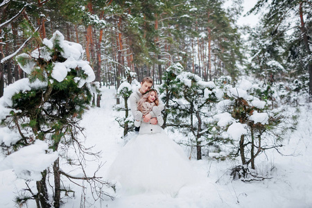 可爱的新婚夫妇米色针织套头衫拥抱在白雪皑皑的森林。冬季婚礼。艺术品