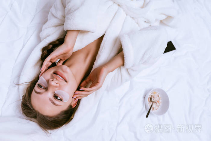 快乐的少女早早醒来, 躺在床上, 下一顿早餐麦片粥, 面带微笑