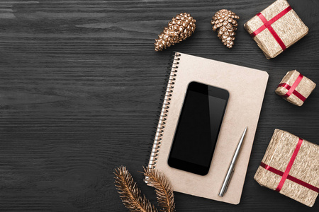 圣诞礼物的顶部视图在一个木制的黑色乡村背景笔记垫笔电话与空间的文字写作和金松锥。
