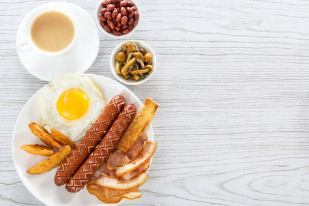 英式早餐，熏香肠，炒鸡蛋，培根，蘑菇，烤面包和豆子。 带牛奶的茶。 早餐在白色盘子上的浅色背景。 文本空间。 上文视