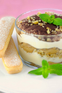 蒂拉米苏传统意大利甜点在一个玻璃在白色盘子上的浅粉色背景与坚果。