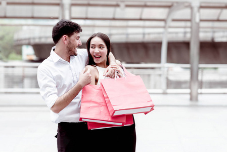 在亚洲国家进行了一天的大减价购物之后，快乐的一对夫妇在交谈。年轻英俊的白人男性和美丽的亚洲女性带着红色的购物袋，看上去非常满意。