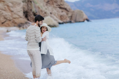快乐的男人拥抱他美丽的女人站在海滩上，背景是悬崖