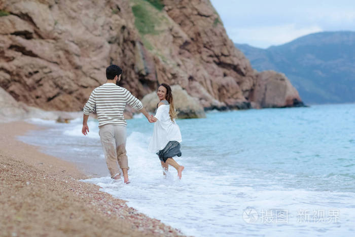 一对快乐的年轻夫妇一起在海边的后景中嬉戏