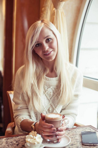女性手拿着一杯热可可。一个年轻的女人坐在一个舒适的咖啡馆里。这个女孩正在喝可可。冬天.舒适的秋季