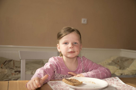 小女孩 playlful 吃巧克力奶油涂在面包上。巧克力甜食品小吃。快乐的女孩在厨房里吃点心。一个可爱的小女孩笑了。一个小女孩