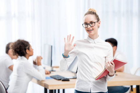 年轻的白种人学生女孩在教室里和朋友挥手