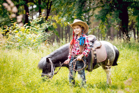 戴着牛仔帽的小女孩带着小马在公园散步
