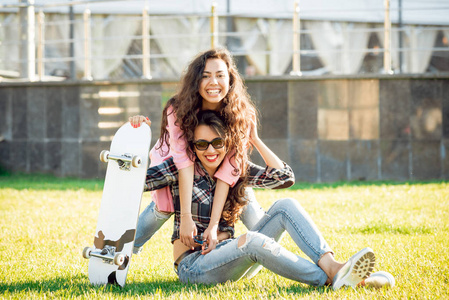 两个穿着休闲服装的年轻混血女孩在绿色草坪上摆着滑板