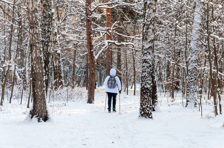 北欧人走。一个穿着白色夹克, 背包在冰冷的森林里徒步旅行的女人。风景秀丽风景与雪