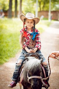 戴着牛仔帽的小女孩骑着小马在公园