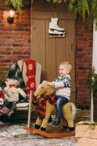 俏皮的微笑的快乐可爱的小男孩穿着毛衣和牛仔裤坐在摇椅在装修的新年房间在家里。圣诞节好心情。生活方式, 家庭和假日2018概念
