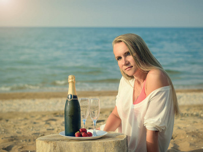 一瓶香槟和一个美丽的女人在海边的盘子里的新鲜草莓
