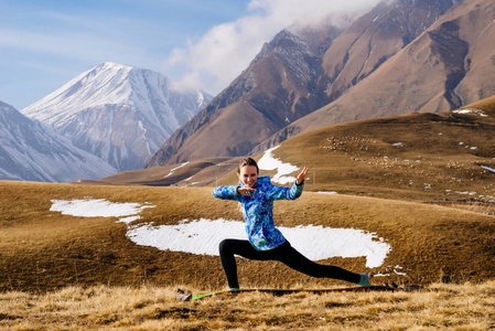 穿着蓝色夹克的女孩在高加索山脉的背景下从事瑜伽, 喜欢旅游