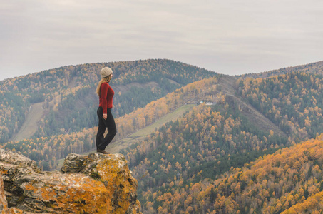 一个穿着红色夹克的女孩在阴天时眺望远处的山上和秋天的森林。 免费文本空间