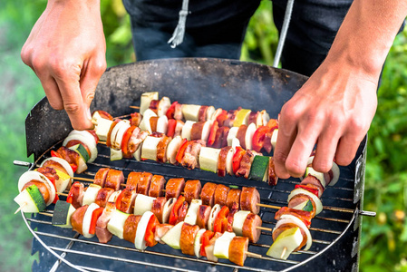 在夏日花园的烧烤炉上烤食物, 厨师的手准备蔬菜和肉串, 露天烧烤在草地上