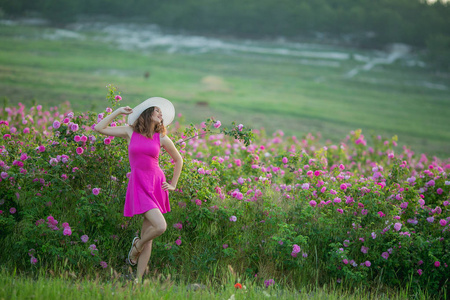 穿紫色连衣裙和白色帽子的年轻女子，玩着鲜花摆姿势