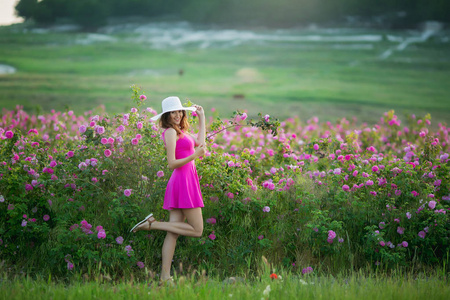 穿紫色连衣裙和白色帽子的年轻女子，玩着鲜花摆姿势