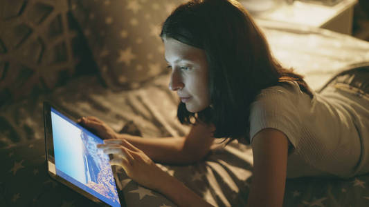 躺在床上的年轻的微笑的妇女看相片从旅行在数字式平板电脑在晚上在家