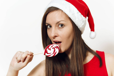美丽的白种人迷人的年轻快乐的女人与健康的皮肤在红色的礼服和圣诞帽在白色背景下拿着棒糖。圣诞老人孤立的关闭。新年假期2018概