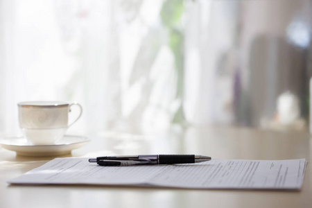 白色咖啡杯的特写，盘子站在桌子上，文件和笔模糊的背景