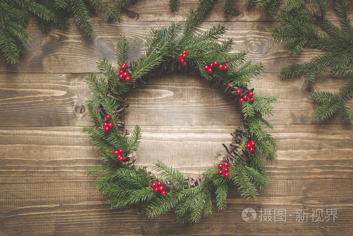 木制木板上的云杉树枝和冬青浆果的圣诞花环。平躺。顶部视图
