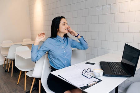 女孩努力疲倦的年轻女孩自由职业者在笔记本电脑上努力工作, 打呵欠
