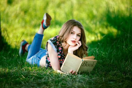 的白种人年轻女孩读书躺在绿草上的树影在夏天。