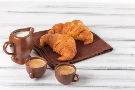 新鲜出炉的牛角面包, 在棕色的餐巾, 奶油, 在白色木制背景的陶瓷菜肴杯咖啡。早餐的新鲜糕点。美味的甜点特写摄影。水平横幅