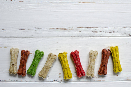 狗骨边框白色木制背景下不同口味的狗的美味咀嚼彩色骨头照片