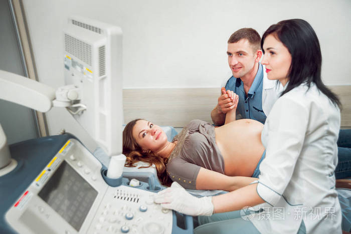 女医生和年轻孕妇与丈夫。 超声波设备。 诊断。 超声波。