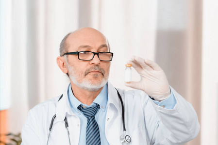 戴眼镜和戴医疗手套的资深医生在诊所看手头药品的画像